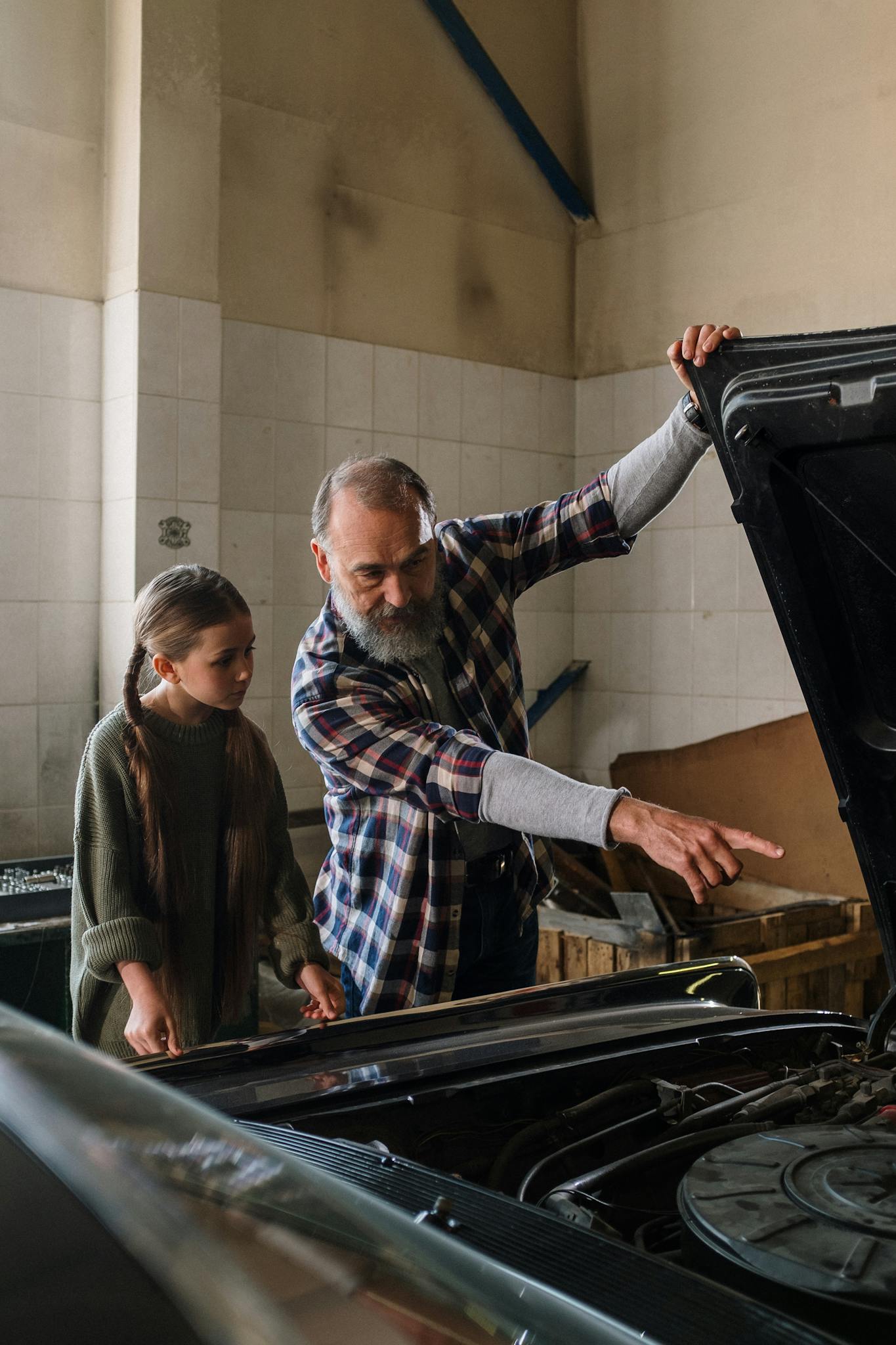 Father teaching daughter about car mechanics in a garage setting.